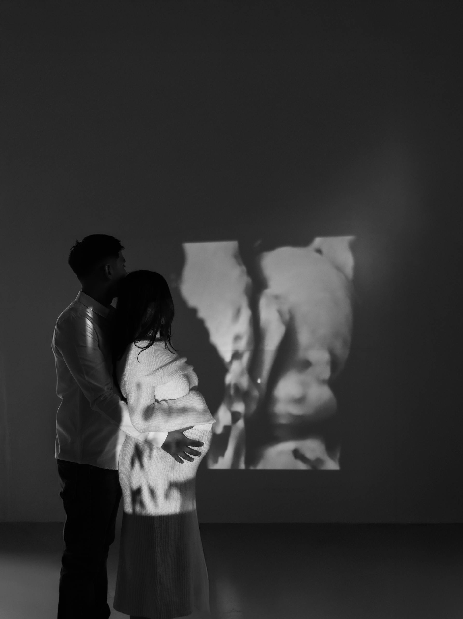 A couple viewing a projected ultrasound image during pregnancy in an intimate, artistic setting.